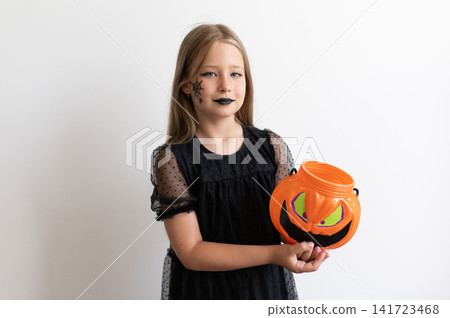 Girl child in witch costume carrying orange trick or treat bucket on white background Girl child in witch costume carrying orange trick or treat bucket on white background 141723468