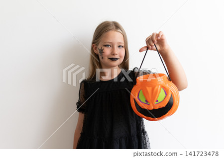 Girl in witch costume holding pumpkin bucket by strap on white background Girl in witch costume holding pumpkin bucket by strap on white background 141723478
