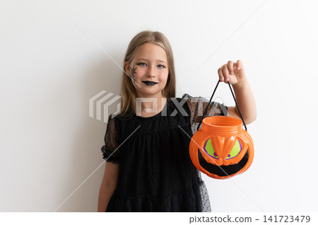 Girl child in witch costume holding pumpkin bucket on white background Girl child in witch costume holding pumpkin bucket on white background 141723479