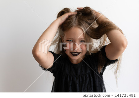 Girl in witch costume messing up her hair and smiling on white background Girl in witch costume messing up her hair and smiling on white background 141723491