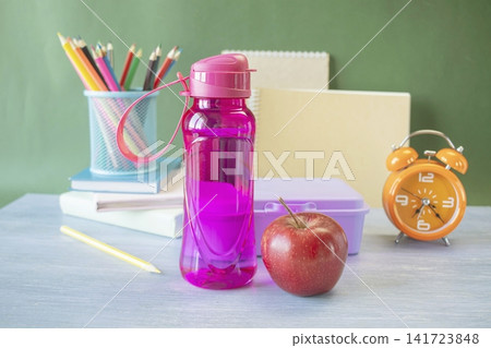 School supplies and healthy lunch on the table for studying. Alarm clock, textbooks, colored pencils and bottle of water and lunch box, back to school concept. School supplies and healthy lunch on the table for studying. Alarm clock, textbooks, colored pencils and bottle of water and lunch box, back to school concept. 141723848