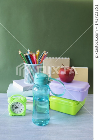 School supplies and healthy lunch on the table for studying. Alarm clock, textbooks, colored pencils and bottle of water and lunch box, back to school concept. School supplies and healthy lunch on the table for studying. Alarm clock, textbooks, colored pencils and bottle of water and lunch box, back to school concept. 141723851