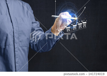 A businessman using a digital stylus to draw a rising growth graph with shopping cart icons on a virtual screen, representing e-commerce success. E-commerce concept A businessman using a digital stylus to draw a rising growth graph with shopping cart icons on a virtual screen, representing e-commerce success. E-commerce concept 141724019