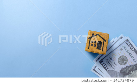A wooden block with a house icon placed on a stack of US hundred-dollar bills, symbolizing real estate investment, property costs, or home financing. Depreciation concept A wooden block with a house icon placed on a stack of US hundred-dollar bills, symbolizing real estate investment, property costs, or home financing. Depreciation concept 141724079