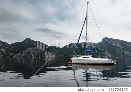 Sailboat on an alpine lake with mountain landscape, illustrating European alpine vacation by the water and summer atmosphere. Sailboat on an alpine lake with mountain landscape, illustrating European alpine vacation by the water and summer atmosphere. 141724135