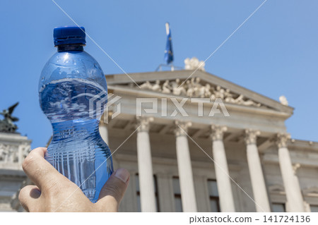 Person holding a plastic water bottle in front of a classical building, symbolizing rising heat and climate change across Europe. 141724136