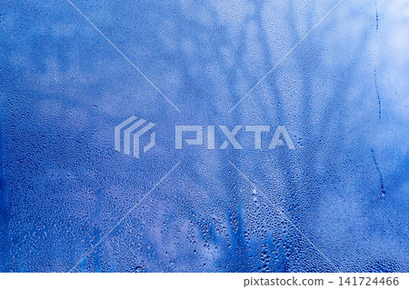 Condensation creates frosty blue texture on clear glass pane. Cold humidity layer displays abstract frozen mist during winter season for creative project. Light condensation offers fresh backdrop 141724466