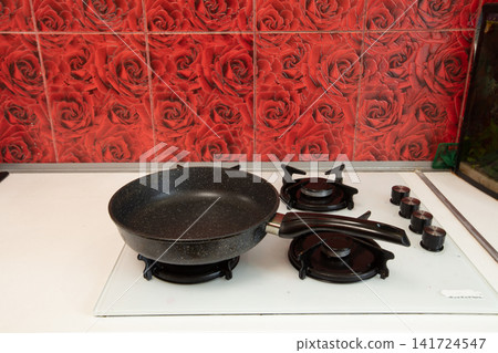 Black pan on gas stove with vibrant red rose tile background, captured with bright natural lighting Black pan on gas stove with vibrant red rose tile background, captured with bright natural lighting 141724547