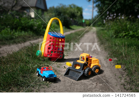 Colorful plastic toy vehicles on a sunlit pathway surrounded by lush greenery and a vibrant toy basket Colorful plastic toy vehicles on a sunlit pathway surrounded by lush greenery and a vibrant toy basket 141724565