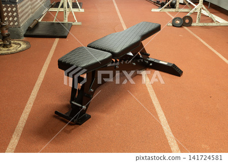Adjustable exercise bench on a rubberized floor in a well-lit workout area Adjustable exercise bench on a rubberized floor in a well-lit workout area 141724581