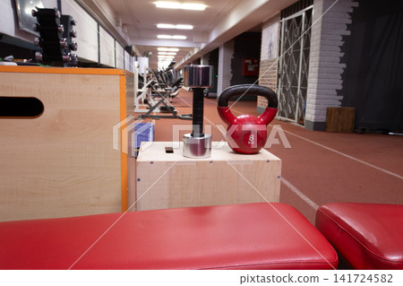 Home gym workout equipment setup with red leather bench, chrome dumbbell, and red kettlebell Home gym workout equipment setup with red leather bench, chrome dumbbell, and red kettlebell 141724582
