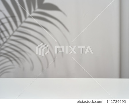 A white, empty tabletop with a soft palm branch shadow against a gray wall. A white, empty tabletop with a soft palm branch shadow against a gray wall. 141724693