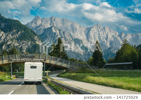 Campervan driving through Planica valley in the Julian Alps, Triglavski narodni park, Slovenia, with green meadows, forest and dramatic rocky mountain backdrop, modern road trip scene Campervan driving through Planica valley in the Julian Alps, Triglavski narodni park, Slovenia, with green meadows, forest and dramatic rocky mountain backdrop, modern road trip scene 141725029