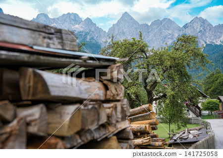 Stacked firewood and village houses in Kranjska Gora, Slovenia, with the rocky Julian Alps in the background, showing everyday alpine life and strong sense of place Stacked firewood and village houses in Kranjska Gora, Slovenia, with the rocky Julian Alps in the background, showing everyday alpine life and strong sense of place 141725058
