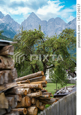 Stacked firewood and village houses in Kranjska Gora, Slovenia, with the rocky Julian Alps in the background, showing everyday alpine life and strong sense of place Stacked firewood and village houses in Kranjska Gora, Slovenia, with the rocky Julian Alps in the background, showing everyday alpine life and strong sense of place 141726017
