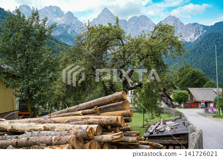 Stacked firewood and village houses in Kranjska Gora, Slovenia, with the rocky Julian Alps in the background, showing everyday alpine life and strong sense of place Stacked firewood and village houses in Kranjska Gora, Slovenia, with the rocky Julian Alps in the background, showing everyday alpine life and strong sense of place 141726021