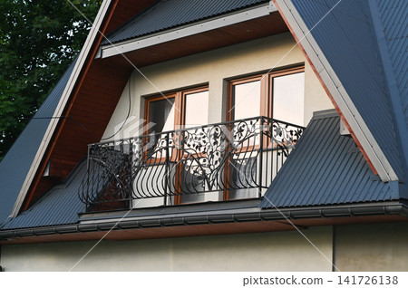House exterior with attic roof and balcony creates cozy residential architecture scene. Home features decorative railing, modern design elements and suburban atmosphere for real estate, lifestyle House exterior with attic roof and balcony creates cozy residential architecture scene. Home features decorative railing, modern design elements and suburban atmosphere for real estate, lifestyle 141726138