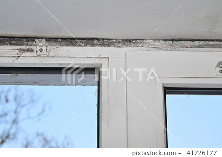 Close-up view of window with visible mold and dirt on frame. Window frame showing signs of mold and dirt accumulation, with detailed view of affected areas, revealing moisture damage. Close-up view of window with visible mold and dirt on frame. Window frame showing signs of mold and dirt accumulation, with detailed view of affected areas, revealing moisture damage. 141726177