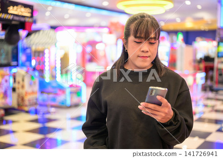 Woman Looking at Smartphone Screen in Arcade Woman Looking at Smartphone Screen in Arcade 141726941