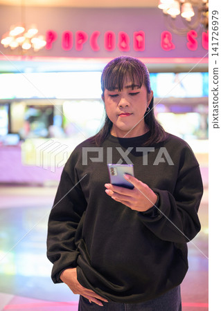 Asian Person Using Mobile Phone in Movie Theater Foyer 141726979