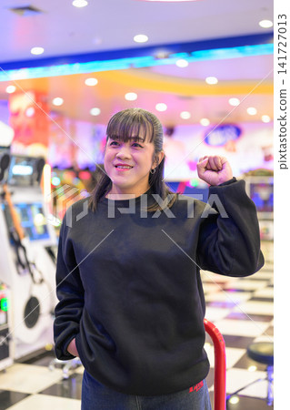 Cheerful Woman Standing Proudly in Vibrant Game Center Cheerful Woman Standing Proudly in Vibrant Game Center 141727013