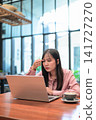 Thoughtful Asian Woman Touching Head while Looking at Laptop 141727270