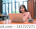 Happy Asian Woman Laughing while Working on Her Laptop in a Cafe 141727271