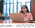 Cheerful Asian Woman Multi-tasking with Phone and Laptop in a Cafe 141727274