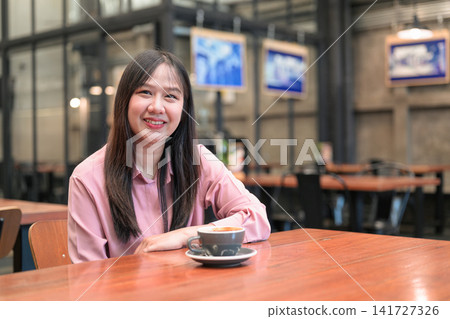 Portrait of a Confident Asian Woman Sitting in a Cafe with a Cup of Coffee Portrait of a Confident Asian Woman Sitting in a Cafe with a Cup of Coffee 141727326