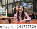 Happy Asian Woman Smiling and Looking Up in a Cafe with a Cup of Coffee 141727329