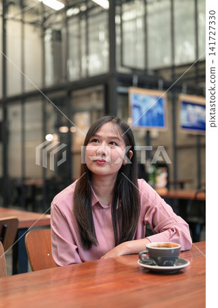 Thoughtful Asian Woman Looking Up while Sitting in a Cafe with Coffee Thoughtful Asian Woman Looking Up while Sitting in a Cafe with Coffee 141727330