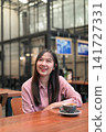 Happy Asian Woman Smiling and Looking Up in a Cafe with a Cup of Coffee 141727331