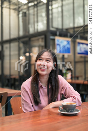 Happy Asian Woman Smiling and Looking Up in a Cafe with a Cup of Coffee Happy Asian Woman Smiling and Looking Up in a Cafe with a Cup of Coffee 141727331