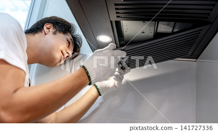Asian male technician removing range metal filter looking at extractor motor inside the cooker hood 141727336
