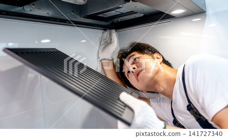 Asian male technician removing range metal filter looking at extractor motor inside the cooker hood Asian male technician removing range metal filter looking at extractor motor inside the cooker hood 141727340