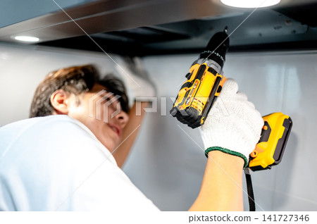Asian male technician using electric screwdriver fixing extractor motor in cooker hood Asian male technician using electric screwdriver fixing extractor motor in cooker hood 141727346