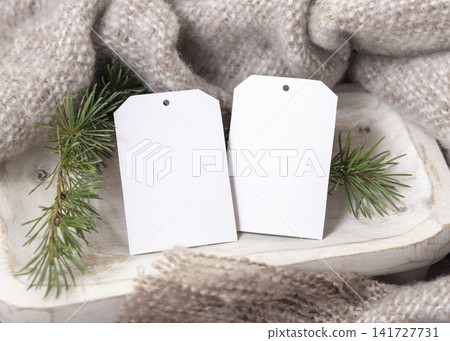 Two vertical gift tag mockup near beige knitted blanket and fir branches. Rustic Christmas packaging Two vertical gift tag mockup near beige knitted blanket and fir branches. Rustic Christmas packaging 141727731