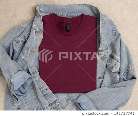 Blank dark red folded t-shirt mockup over blue denim jacket, crewneck template for print on demand Blank dark red folded t-shirt mockup over blue denim jacket, crewneck template for print on demand 141727741