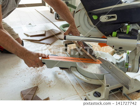 Construction worker cutting oak parquet planks with miter saw during hardwood floor installation Construction worker cutting oak parquet planks with miter saw during hardwood floor installation 141727742