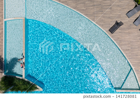 Two kids relax at the edge of clear blue pool during sunny summer vacation. This aerial view captures family,  friends, fun, and recreation at resort, relaxation and joyful outdoor moments. 141728081
