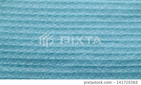 Close up of pastel blue waffle weave fabric with a soft, raised square grid design creating a three dimensional, pillowy surface. 141728368