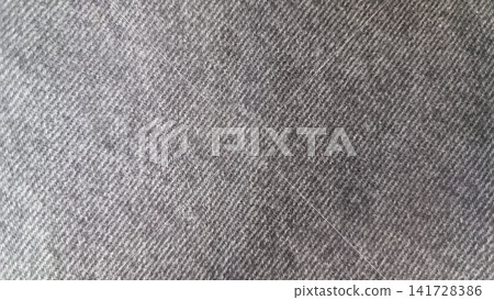 Close up of gray denim with a diagonal twill weave and faded, worn surface. Close up of gray denim with a diagonal twill weave and faded, worn surface. 141728386