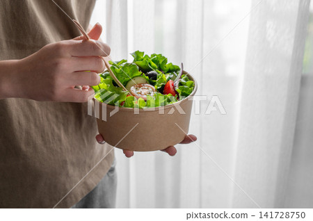 A woman holds a healthy vegetable salad in an eco-friendly takeaway bowl. A woman holds a healthy vegetable salad in an eco-friendly takeaway bowl. 141728750