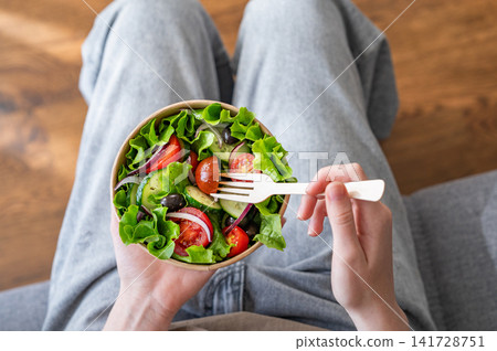 A woman holds a healthy vegetable salad in an eco-friendly takeaway bowl. A woman holds a healthy vegetable salad in an eco-friendly takeaway bowl. 141728751