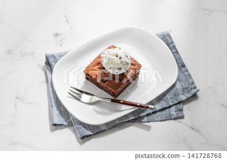 A piece of chocolate brownie with ice cream on a plate on a light marble background A piece of chocolate brownie with ice cream on a plate on a light marble background 141728768