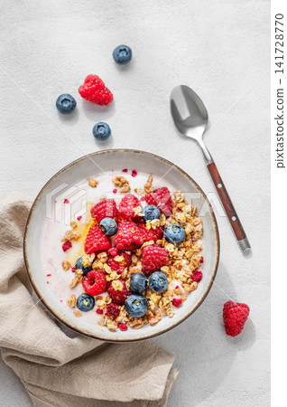 Natural yogurt with granola, blueberry and raspberry in a bowl on a light background Natural yogurt with granola, blueberry and raspberry in a bowl on a light background 141728770