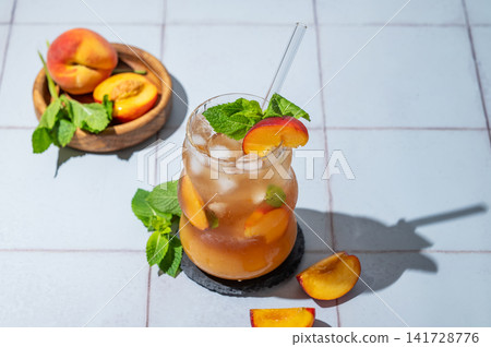 Refreshing peach iced cocktail or tea with mint in a glass on a tile background with shadow. 141728776