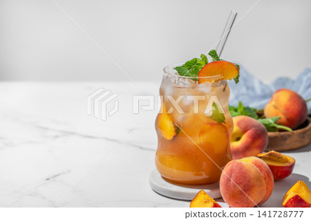 Refreshing peach iced cocktail or tea with mint in a glass on a light background with shadow. Refreshing peach iced cocktail or tea with mint in a glass on a light background with shadow. 141728777
