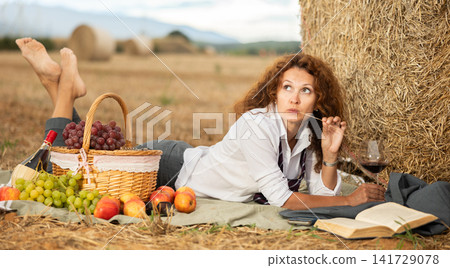Woman in white blouse in office clothes, lying on blanket and reading book. Picnic on farm field Woman in white blouse in office clothes, lying on blanket and reading book. Picnic on farm field 141729078