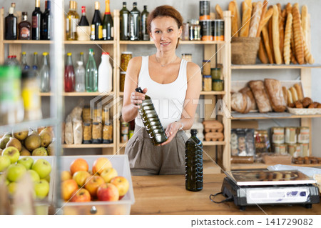 Sales woman selling bottles of olive oil in grocery department of supermarket Sales woman selling bottles of olive oil in grocery department of supermarket 141729082